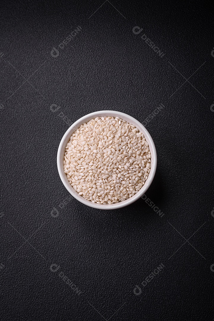 Arroz branco cru em uma tigela redonda de cerâmica sobre um fundo escuro de concreto. Cozinhar comida asiática