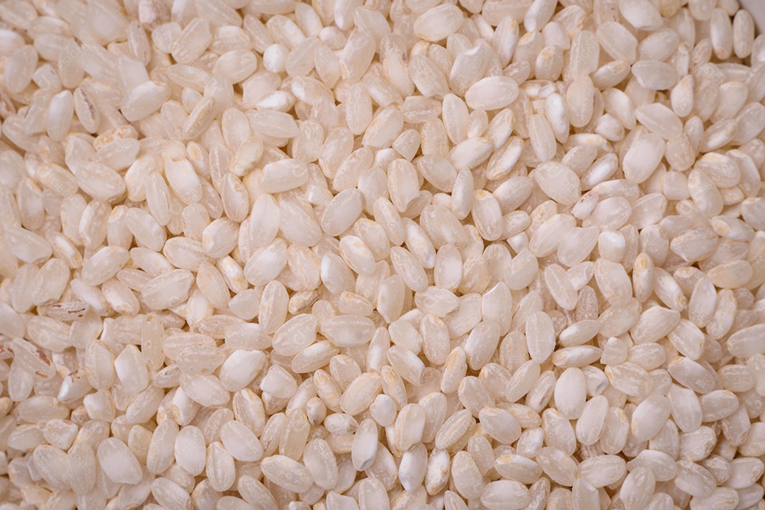 Arroz branco cru em uma tigela redonda de cerâmica sobre um fundo escuro de concreto. Cozinhar comida asiática