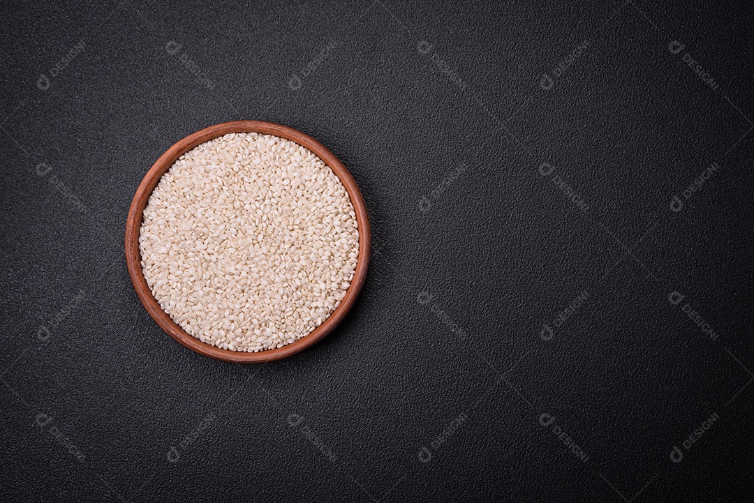 Arroz branco cru em uma tigela redonda de cerâmica sobre um fundo escuro de concreto. Cozinhar comida asiática