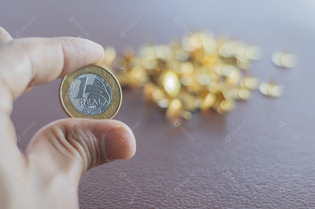 1 moeda real, dinheiro brasileiro com peças de ouro ao fundo