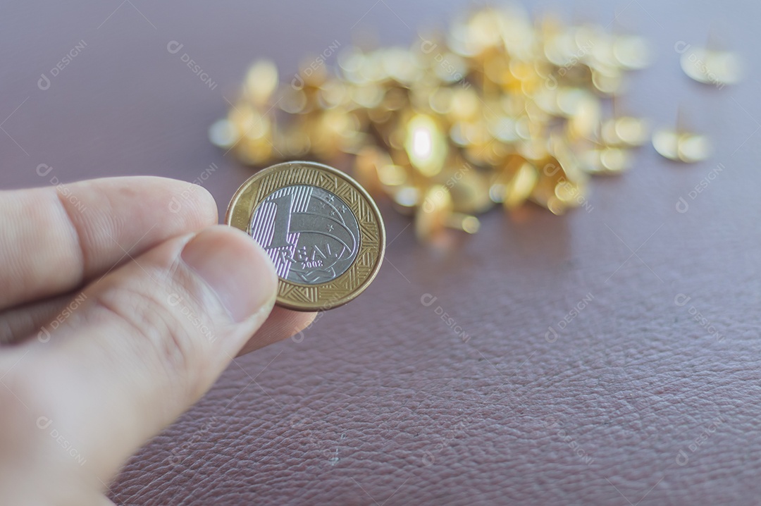 1 moeda real, dinheiro brasileiro com peças de ouro ao fundo