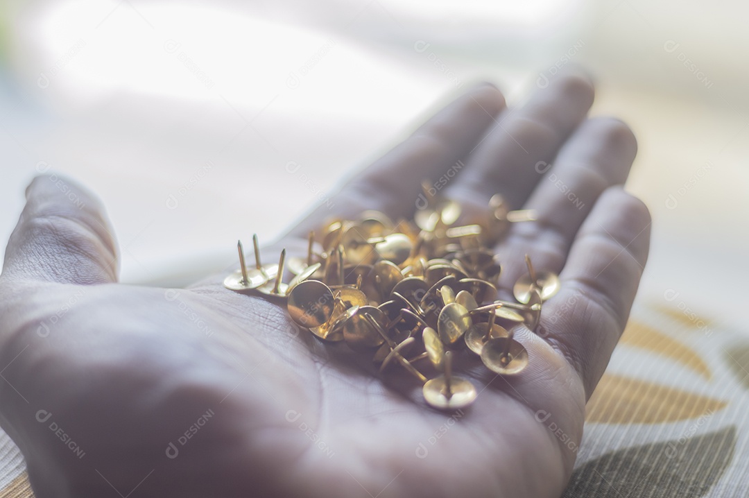 Alfinetes dourados com luz natural e uma mão masculina segurando.