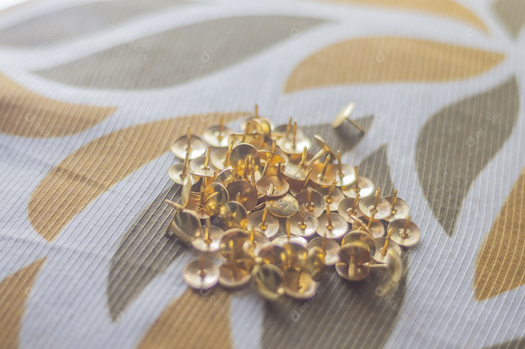 Alfinetes dourados com luz natural e uma mão masculina segurando.