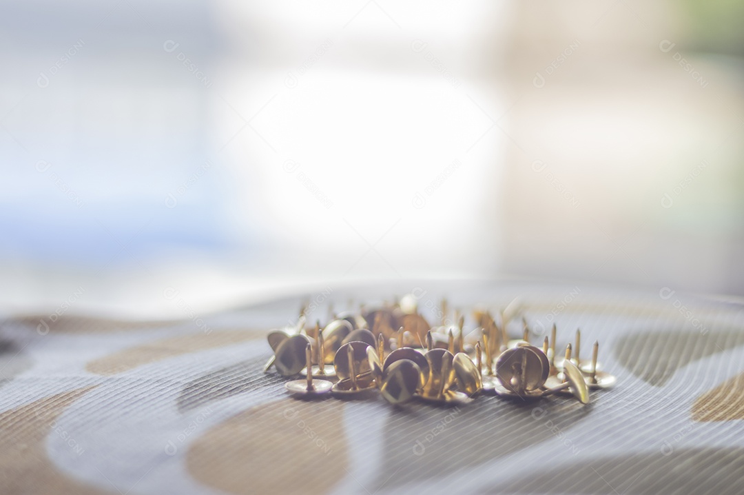 Alfinetes dourados com luz natural e uma mão masculina segurando.