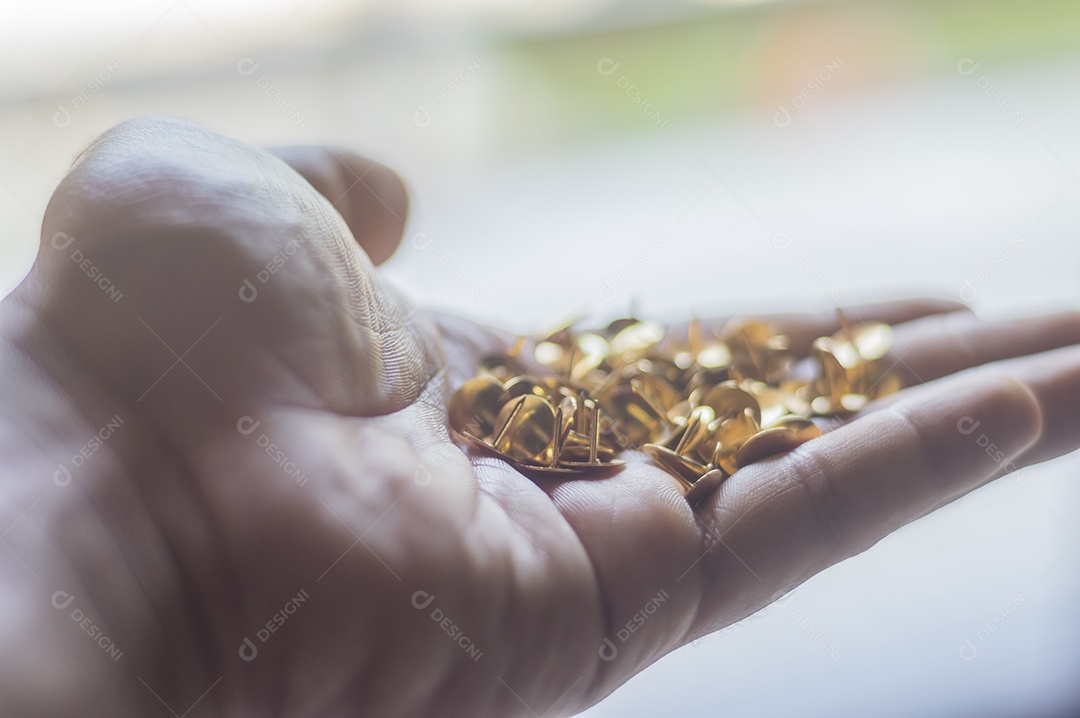 Alfinetes dourados com luz natural e uma mão masculina segurando.