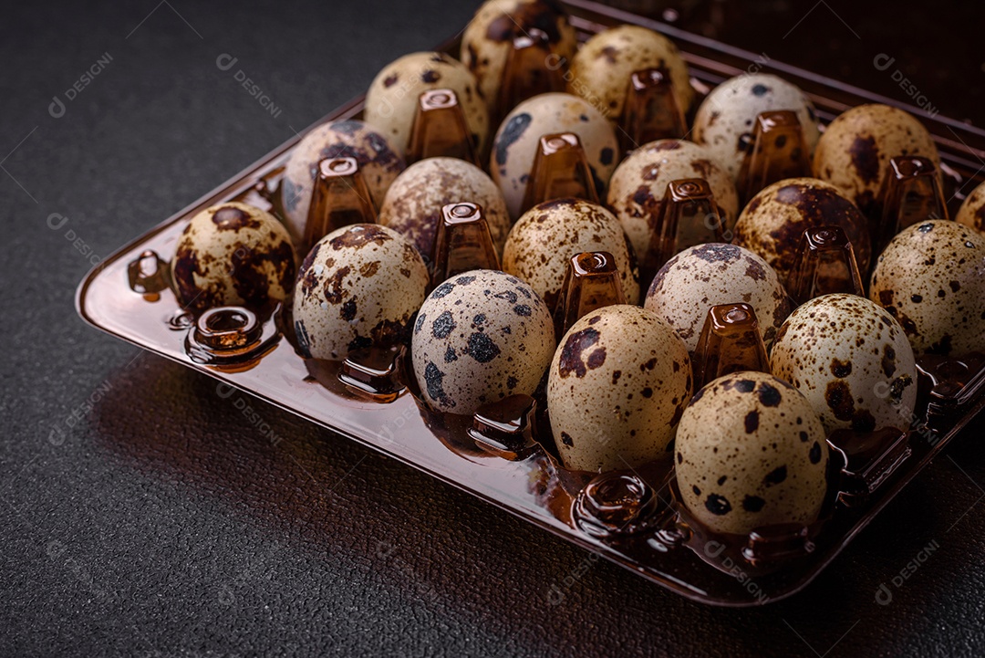 Ovos de codorna crus em uma caixa de plástico sobre um fundo escuro de concreto.