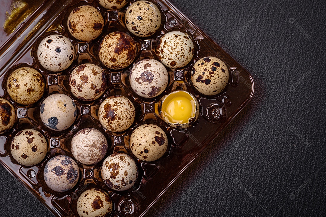 Ovos de codorna crus em uma caixa de plástico sobre um fundo escuro de concreto.