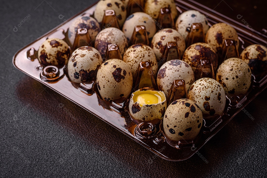 Ovos de codorna crus em uma caixa de plástico sobre um fundo escuro de concreto.