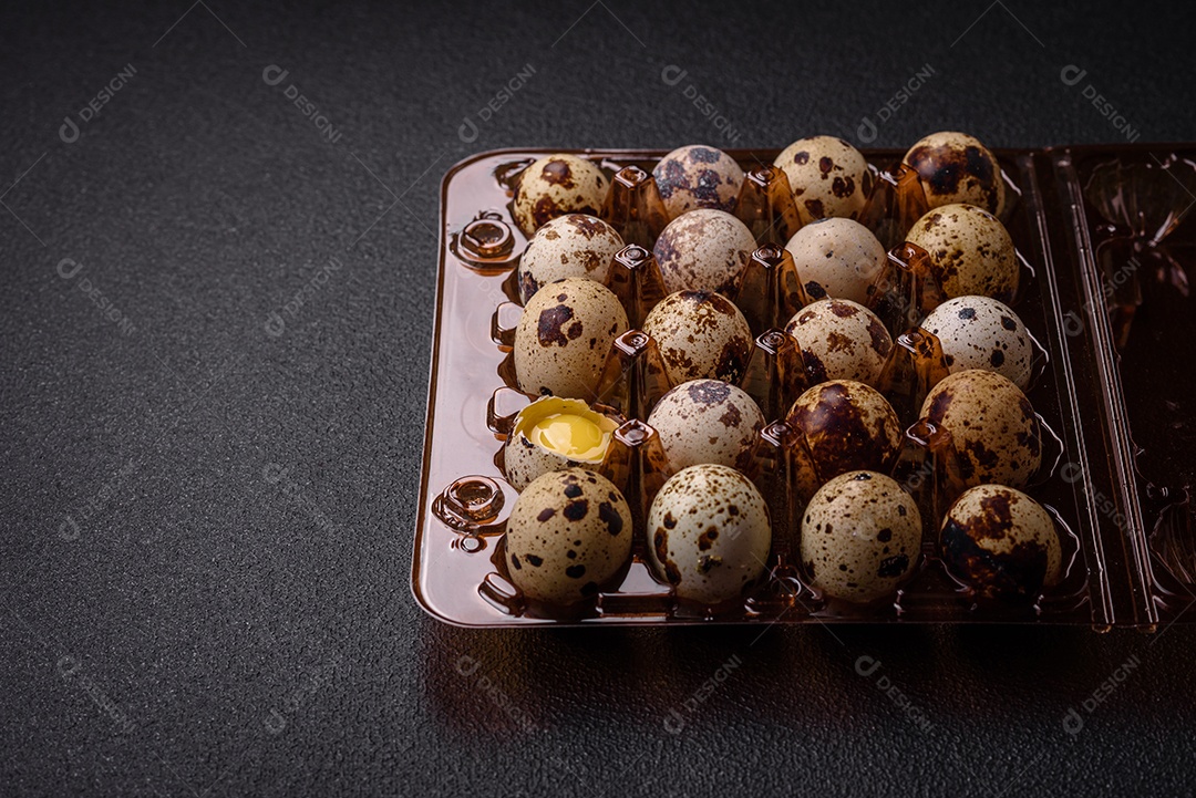 Ovos de codorna crus em uma caixa de plástico sobre um fundo escuro de concreto.