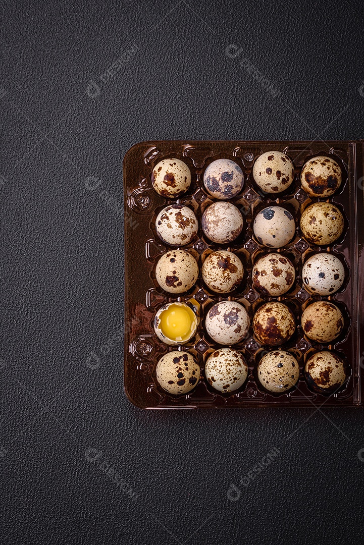 Ovos de codorna crus em uma caixa de plástico sobre um fundo escuro de concreto.