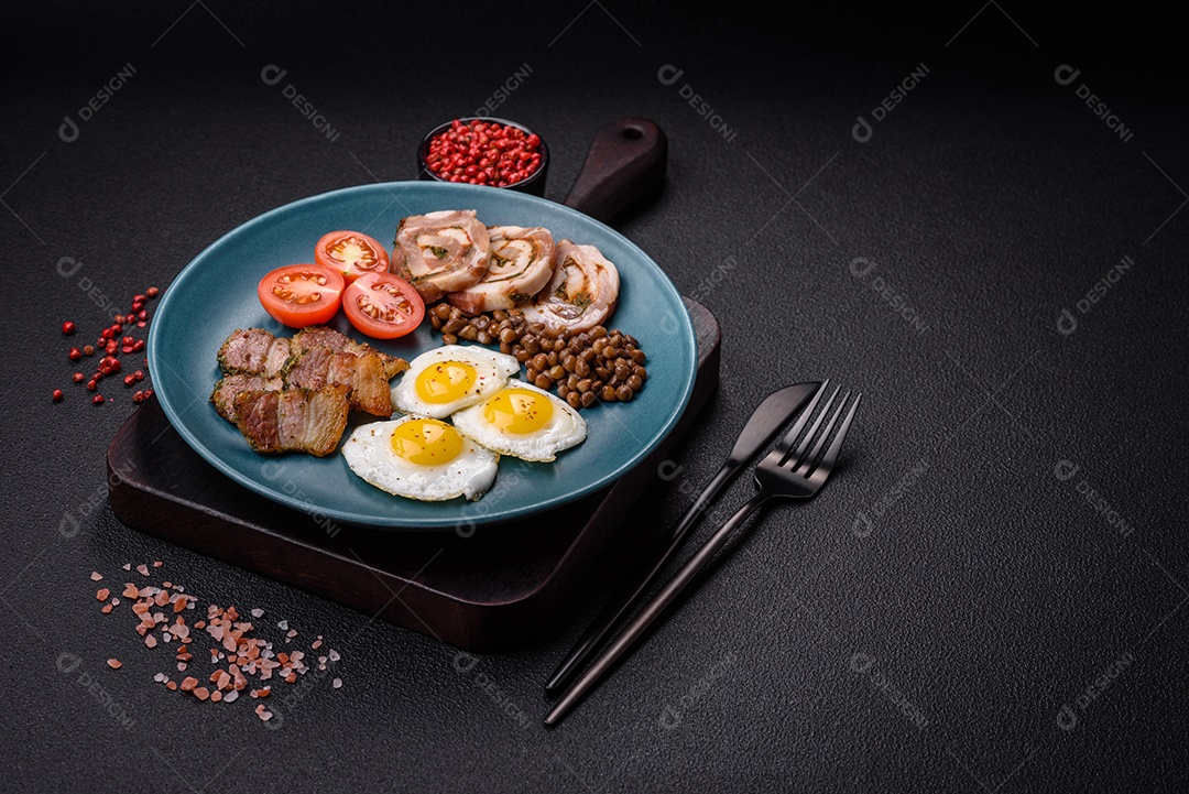 Delicioso café da manhã nutritivo com ovos de codorna fritos, bacon, legumes e tomate cereja com sal, especiarias e ervas em um fundo escuro de concreto
