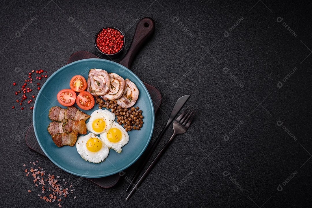 Delicioso café da manhã nutritivo com ovos de codorna fritos, bacon, legumes e tomate cereja com sal, especiarias e ervas em um fundo escuro de concreto