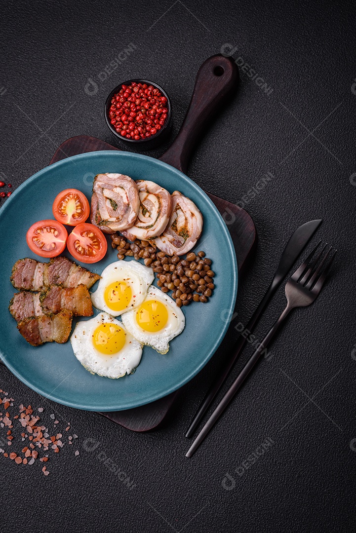 Delicioso café da manhã nutritivo com ovos de codorna fritos, bacon, legumes e tomate cereja com sal, especiarias e ervas em um fundo escuro de concreto