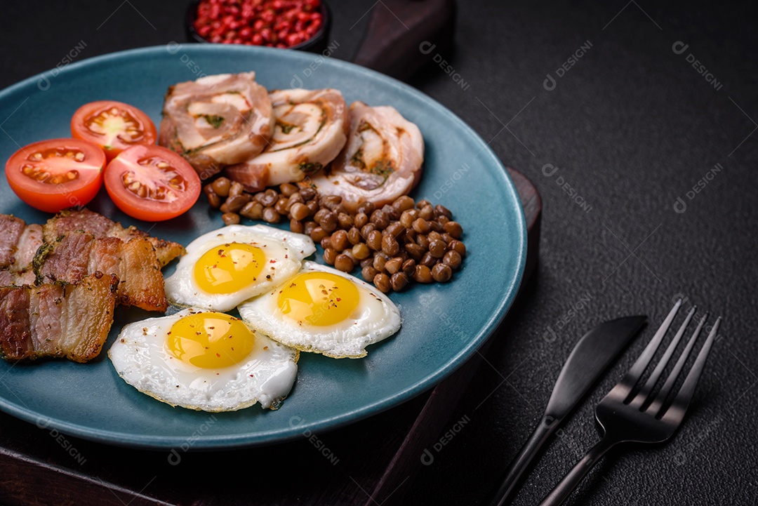 Delicioso café da manhã nutritivo com ovos de codorna fritos, bacon, legumes e tomate cereja com sal, especiarias e ervas em um fundo escuro de concreto
