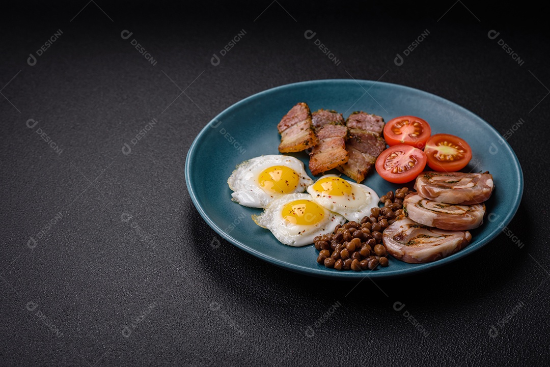 Delicioso café da manhã nutritivo com ovos de codorna fritos, bacon, legumes e tomate cereja com sal, especiarias e ervas em um fundo escuro de concreto