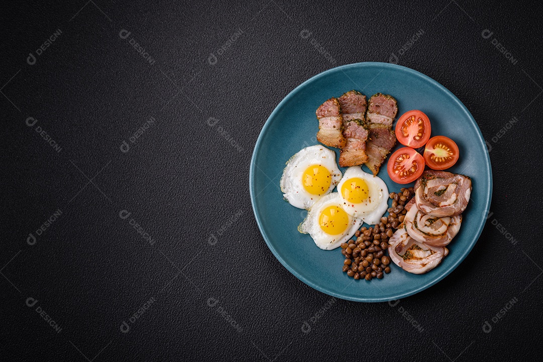Delicioso café da manhã nutritivo com ovos de codorna fritos, bacon, legumes e tomate cereja com sal, especiarias e ervas em um fundo escuro de concreto