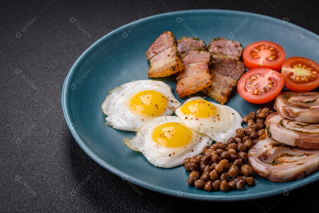 Delicioso café da manhã nutritivo com ovos de codorna fritos, bacon, legumes e tomate cereja com sal, especiarias e ervas em um fundo escuro de concreto