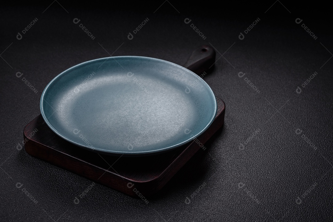 Placa cerâmica vazia e acidentada em um fundo de concreto texturizado. Utensílio de cozinha