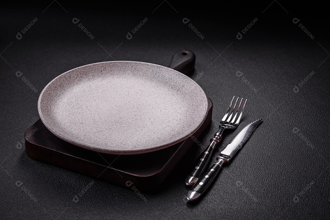 Placa cerâmica vazia e acidentada em um fundo de concreto texturizado. Utensílio de cozinha