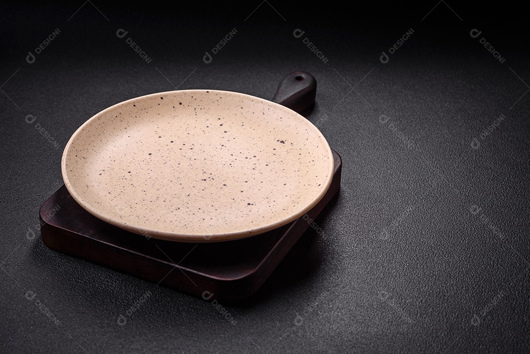 Placa cerâmica vazia e acidentada em um fundo de concreto texturizado. Utensílio de cozinha