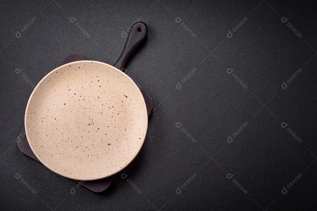 Placa cerâmica vazia e acidentada em um fundo de concreto texturizado. Utensílio de cozinha