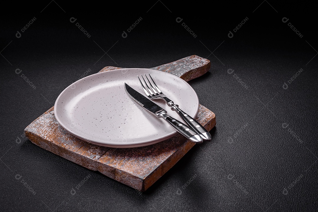 Placa cerâmica vazia e acidentada em um fundo de concreto texturizado. Utensílio de cozinha