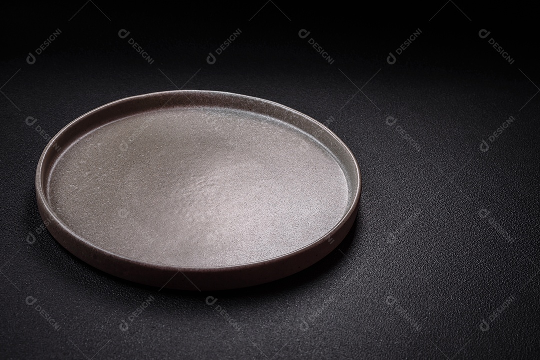 Placa cerâmica vazia e acidentada em um fundo de concreto texturizado. Utensílio de cozinha