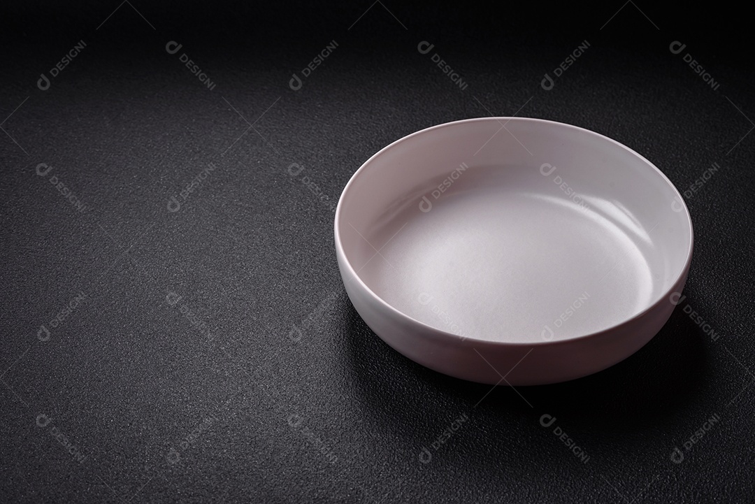 Placa cerâmica vazia e acidentada em um fundo de concreto texturizado. Utensílio de cozinha