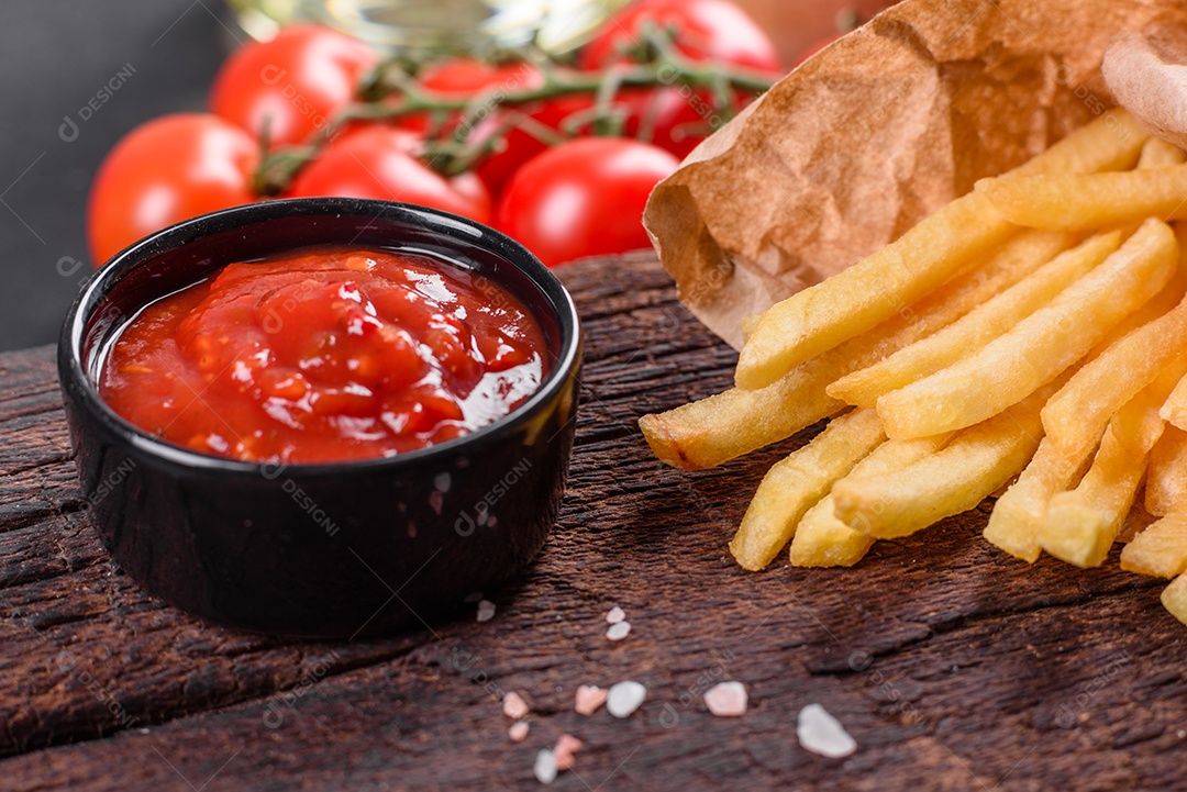 Frescas saborosas batatas fritas e molho vermelho em uma tábua de madeira. Alimentos não saudáveis