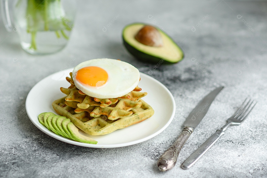 Pequeno-almoço fresco, delicioso e nutritivo com waffles com espinafre, ovo frito e pedaços de abacate