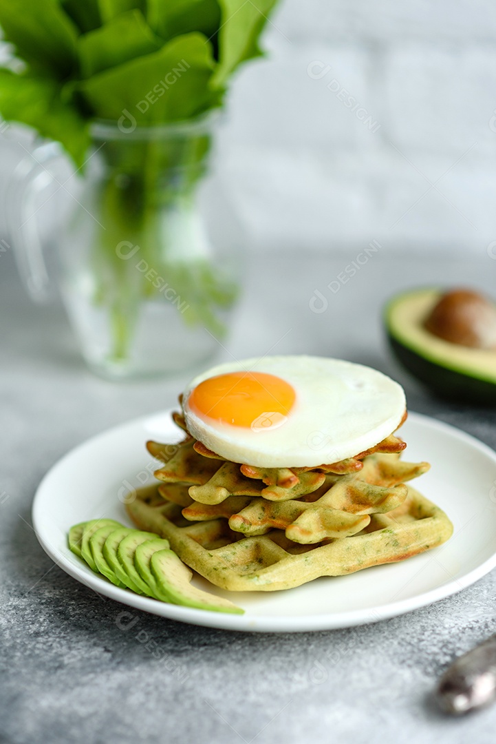 Pequeno-almoço fresco, delicioso e nutritivo com waffles com espinafre, ovo frito e pedaços de abacate