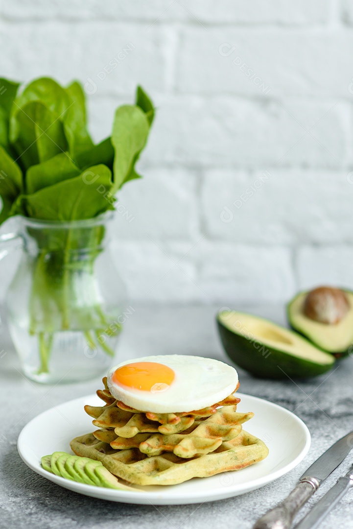 Pequeno-almoço fresco, delicioso e nutritivo com waffles com espinafre, ovo frito e pedaços de abacate