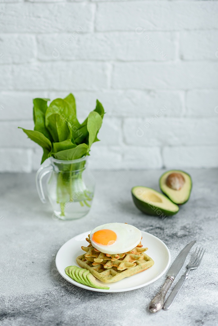 Pequeno-almoço fresco, delicioso e nutritivo com waffles com espinafre, ovo frito e pedaços de abacate