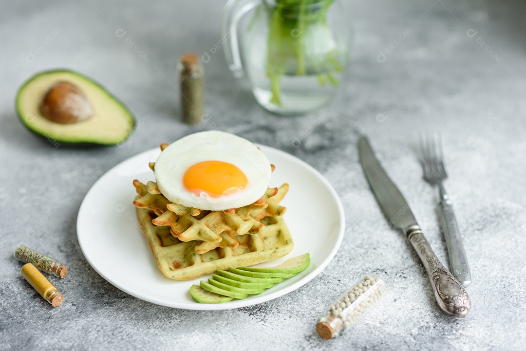 Pequeno-almoço fresco, delicioso e nutritivo com waffles com espinafre, ovo frito e pedaços de abacate