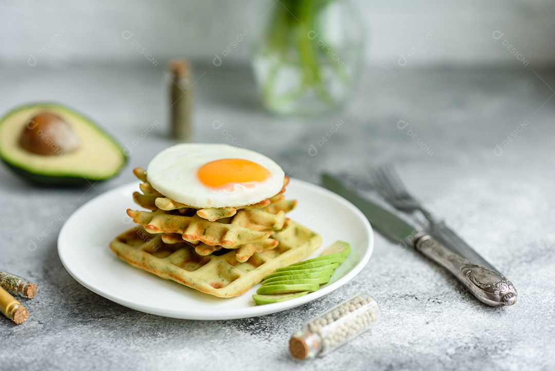 Pequeno-almoço fresco, delicioso e nutritivo com waffles com espinafre, ovo frito e pedaços de abacate