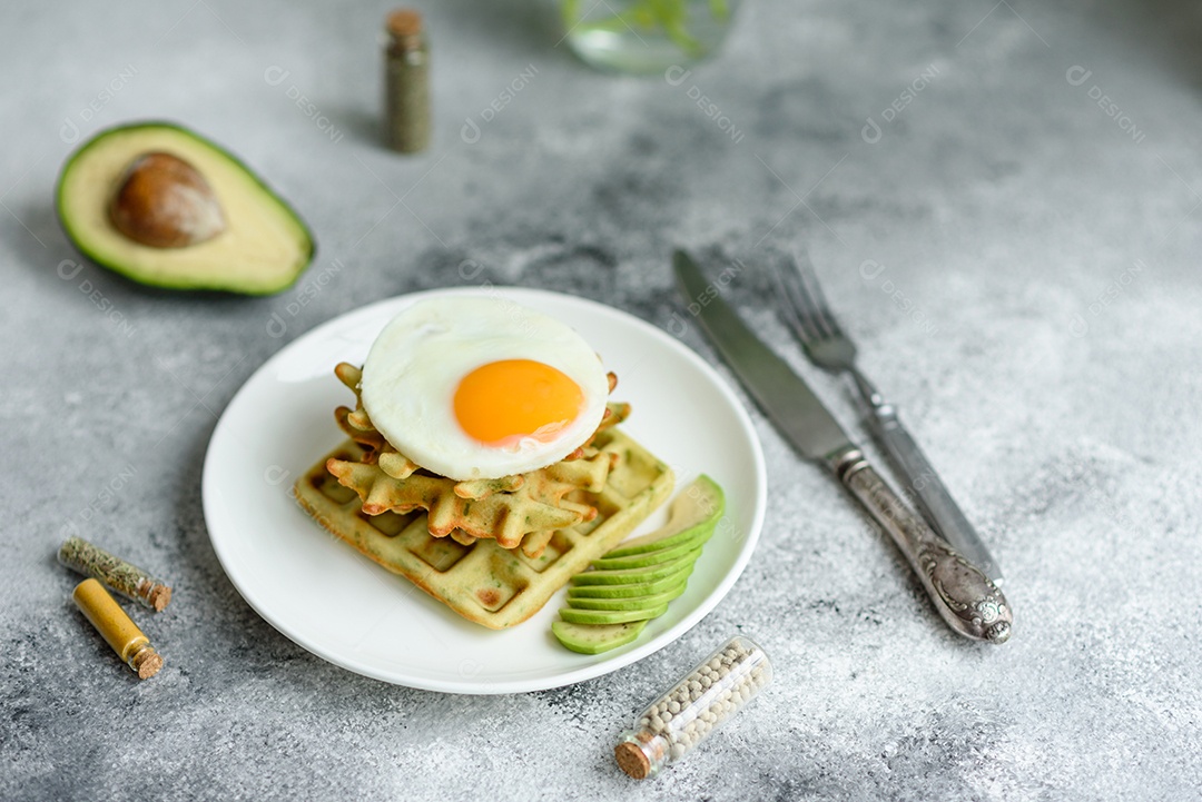 Pequeno-almoço fresco, delicioso e nutritivo com waffles com espinafre, ovo frito e pedaços de abacate