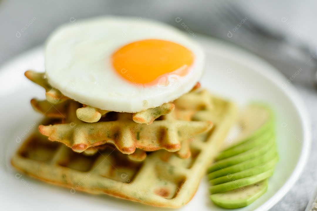 Pequeno-almoço fresco, delicioso e nutritivo com waffles com espinafre, ovo frito e pedaços de abacate