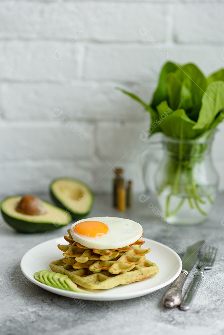 Pequeno-almoço fresco, delicioso e nutritivo com waffles com espinafre, ovo frito e pedaços de abacate