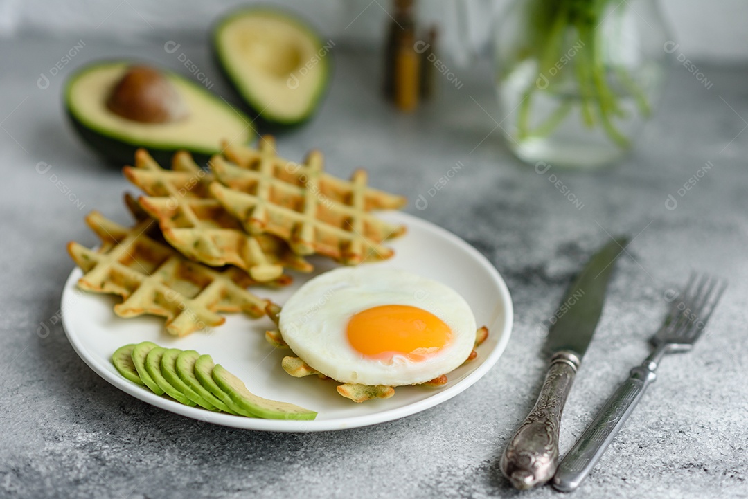 Pequeno-almoço fresco, delicioso e nutritivo com waffles com espinafre, ovo frito e pedaços de abacate