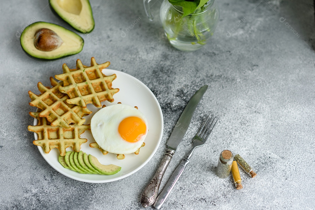 Pequeno-almoço fresco, delicioso e nutritivo com waffles com espinafre, ovo frito e pedaços de abacate
