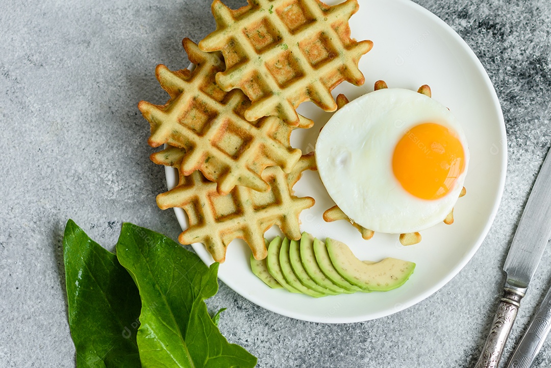 Pequeno-almoço fresco, delicioso e nutritivo com waffles com espinafre, ovo frito e pedaços de abacate
