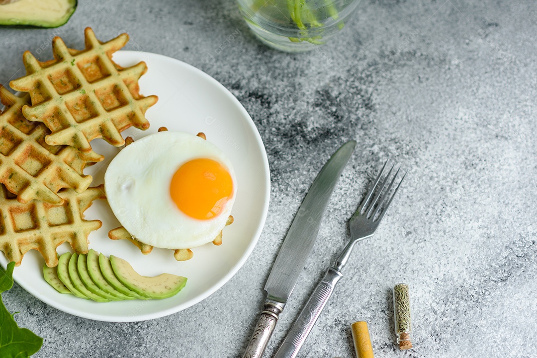 Pequeno-almoço fresco, delicioso e nutritivo com waffles com espinafre, ovo frito e pedaços de abacate