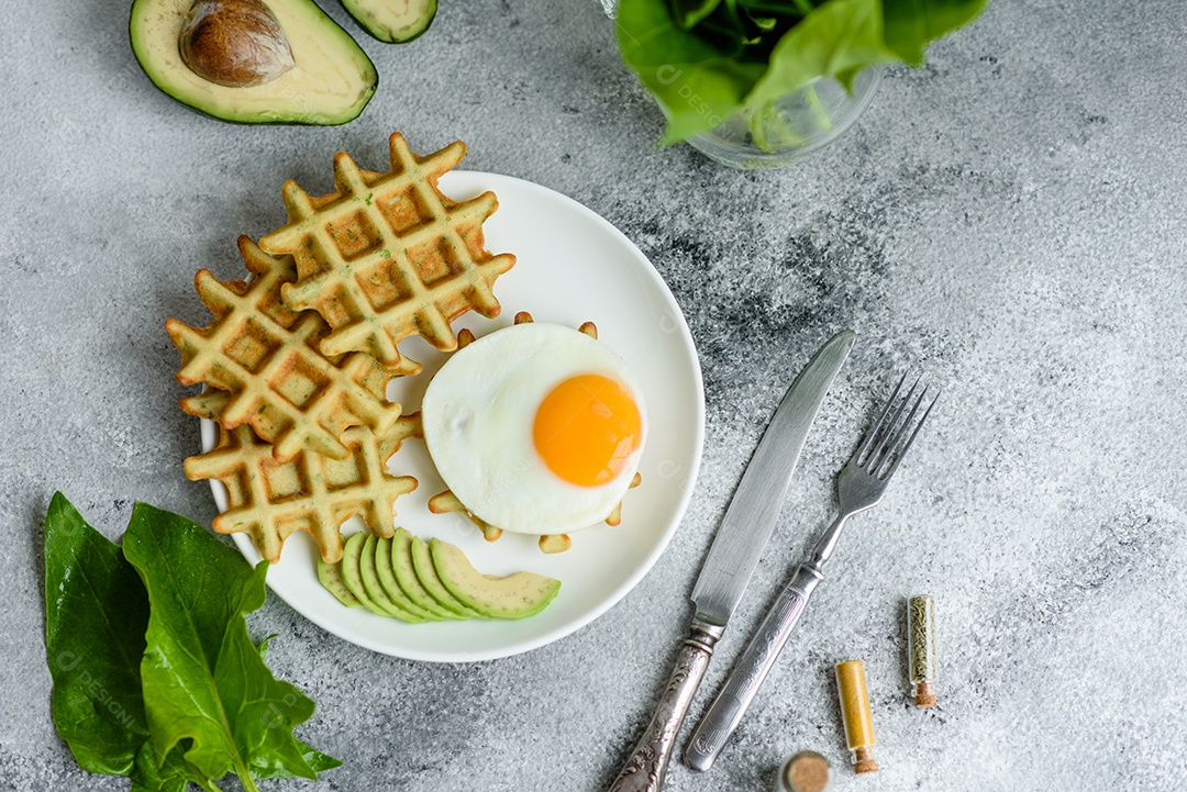 Pequeno-almoço fresco, delicioso e nutritivo com waffles com espinafre, ovo frito e pedaços de abacate