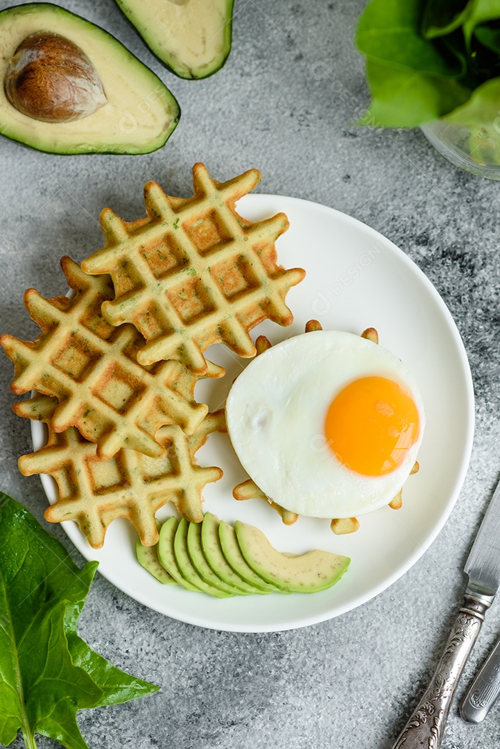 Pequeno-almoço fresco, delicioso e nutritivo com waffles com espinafre, ovo frito e pedaços de abacate