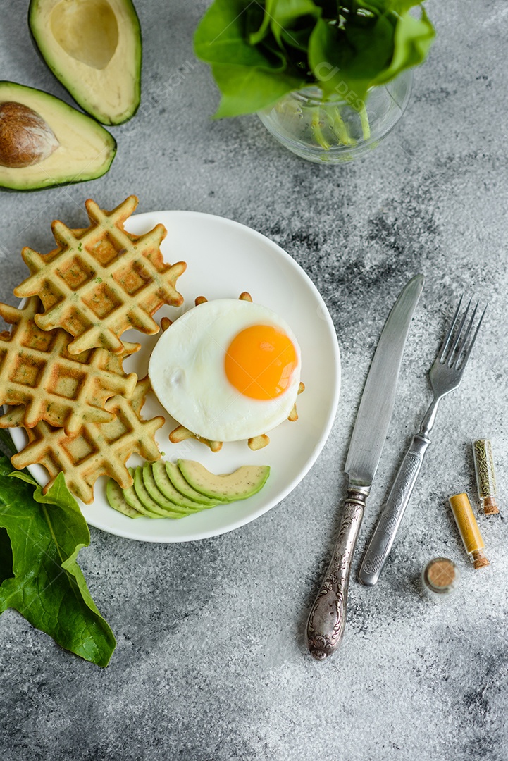 Pequeno-almoço fresco, delicioso e nutritivo com waffles com espinafre, ovo frito e pedaços de abacate