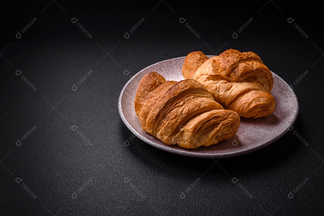 Deliciosos croissants doces assados ​​e crocantes com recheio em uma placa de cerâmica sobre um fundo escuro de concreto