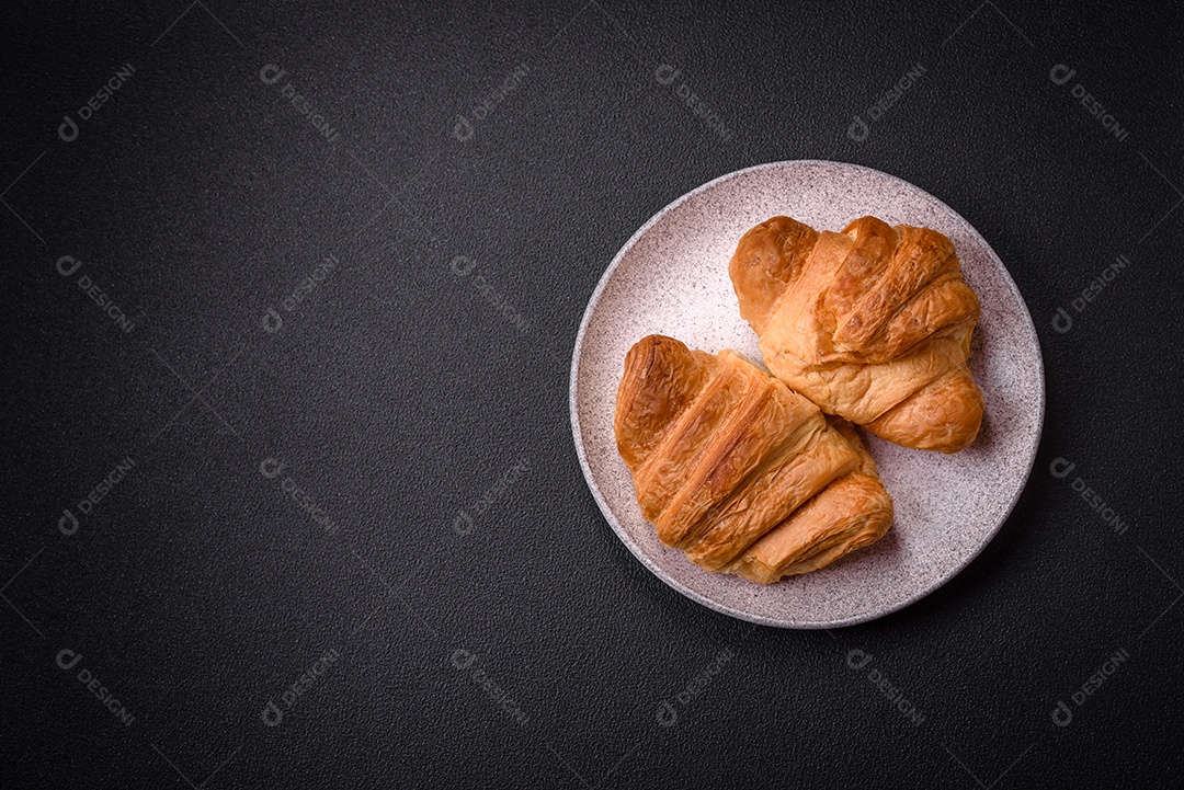 Deliciosos croissants doces assados ​​e crocantes com recheio em uma placa de cerâmica sobre um fundo escuro de concreto