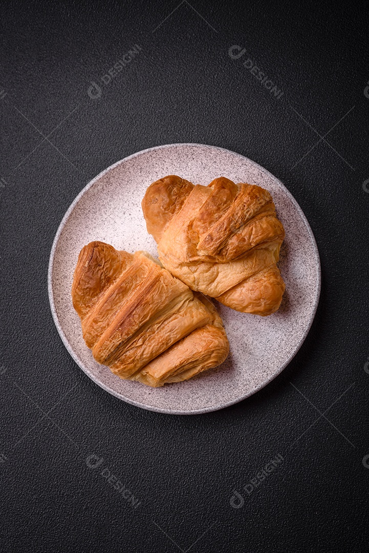 Deliciosos croissants doces assados ​​e crocantes com recheio em uma placa de cerâmica sobre um fundo escuro de concreto