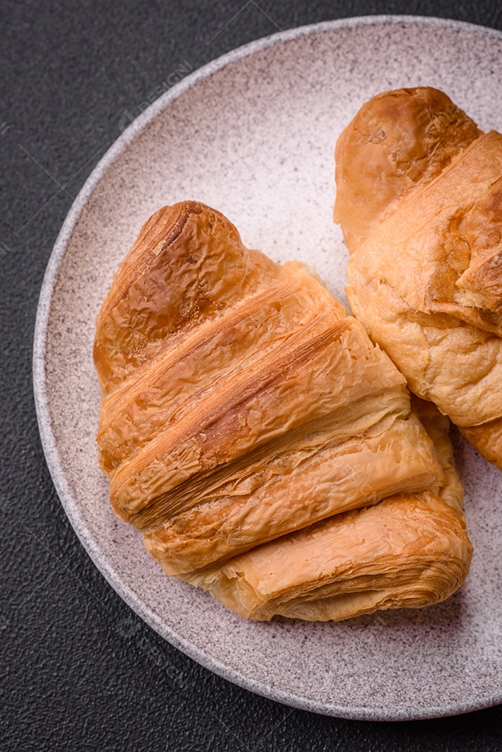 Deliciosos croissants doces assados ​​e crocantes com recheio em uma placa de cerâmica sobre um fundo escuro de concreto