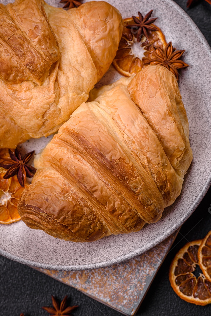 Deliciosos croissants doces assados ​​e crocantes com recheio em uma placa de cerâmica sobre um fundo escuro de concreto